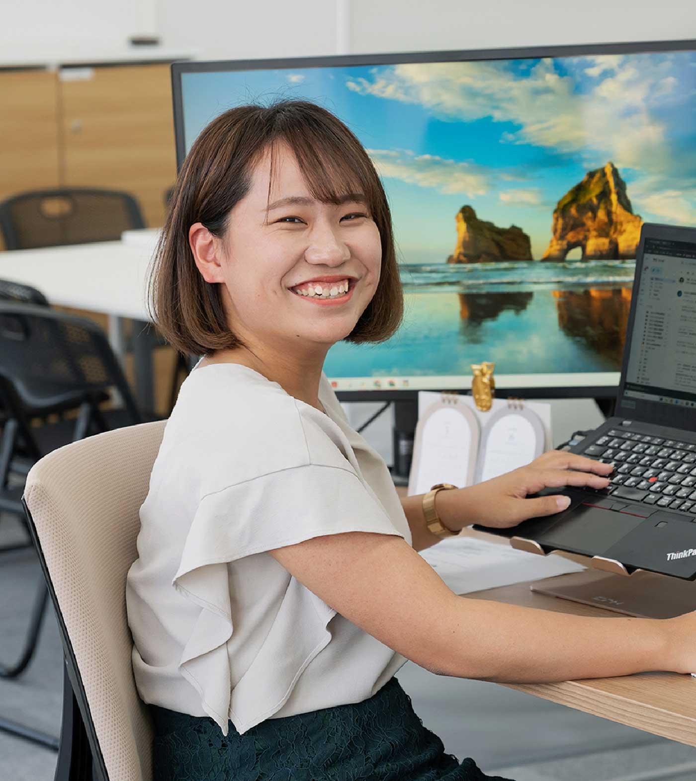 パソコンの前で振り返って笑っているパンクチュアルの女性社員