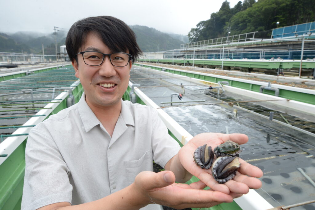 火災時に生き残り、順調に育つアワビを手にする古川専務